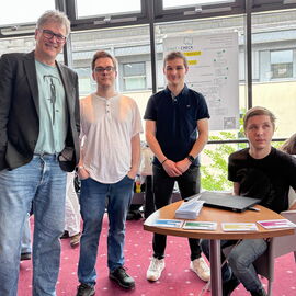 Otfrid Altfeld steht mit den drei Preisträgern im Cineplex vor einem Plakat, das über ihr Projekt informiert.
