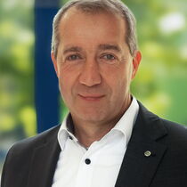 Portraitfoto Patrick Temmesfeld - er hat kurzes Haar und trägt ein schwarzes Sakko auf einem weißen Hemd mit dunklen Knöpfen.